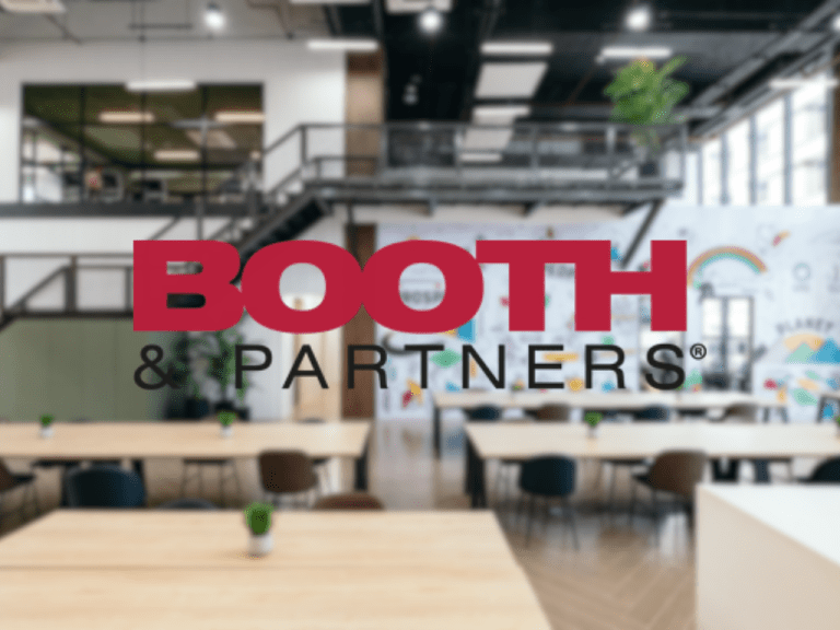 Blurry open-plan office or coworking space with wooden tables and small potted plants. A large, bold red logo reading ‘BOOTH’ overlaps the scene, followed by smaller black text ‘& PARTNERS’ below. The background includes bright lighting, glass walls, and a modern, industrial interior.