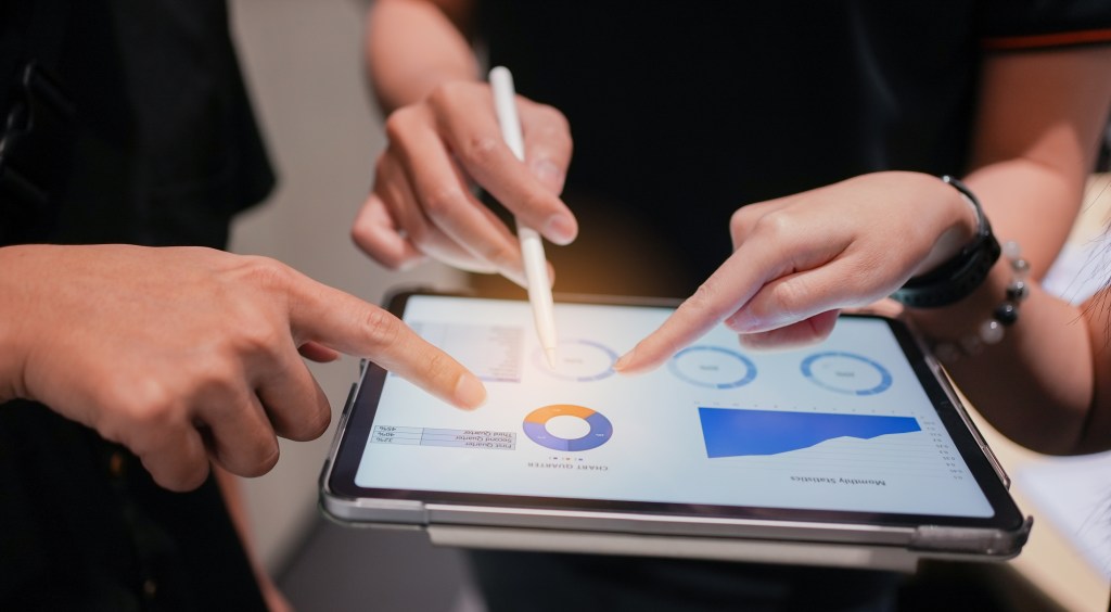 three people pointing on a graph displayed on a tablet