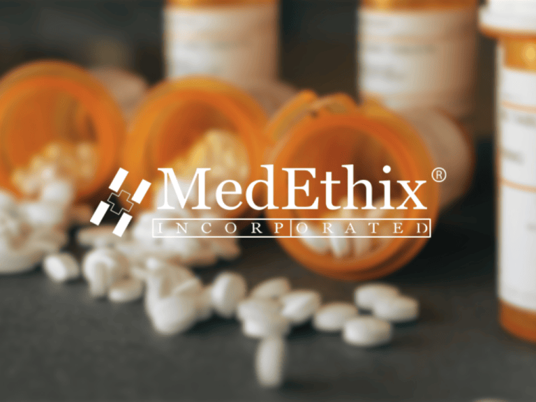 Blurred background of medicine bottles and scattered white pills. A prominent white logo in the center reads ‘MedEthix Incorporated’ with a small geometric motif to the left. The overall impression is of a pharmaceutical branding scene with a soft focus.