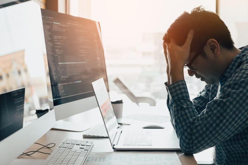 Frustrated employee working at multiple computers while dealing with outdated business software and inefficient processes