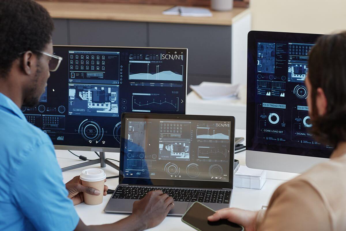 Business professionals reviewing multiple digital dashboards and software systems on computer screens