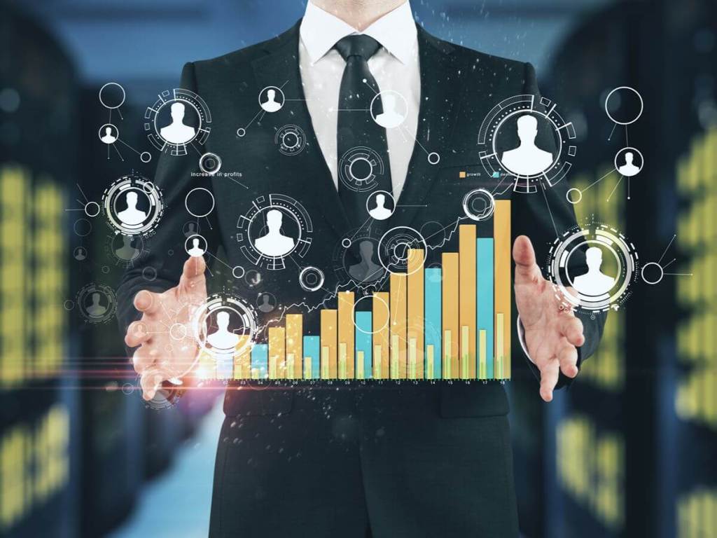 A businessman holding his hands open around glowing digital bar charts and user profile icons.