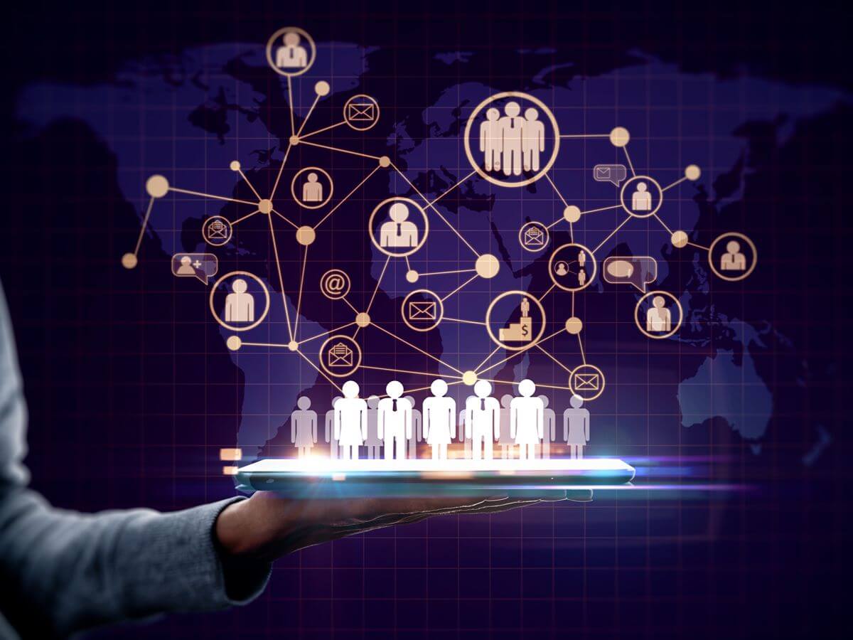 A hand holding a tablet displaying a 3D line-connected network of human avatars, message icons, and contact nodes set against a dark world map background.